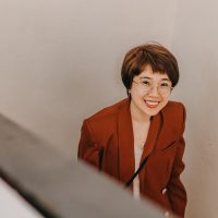 一位短发女性编辑在窗边用平板查看汇率走势图，暖色窗帘与绿植入镜，氛围安静专注